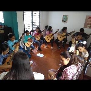 Kinder sitzen in der Runde in einem Raum und spielen Gitarre