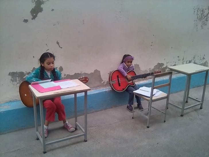 Zwei Mädchen sitzen auf einem Mauerchen und spielen Gitarre